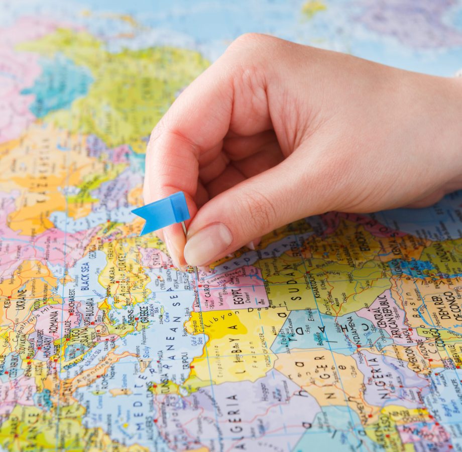 Travelling background. Hand tackling county on the map Travelling background. Female hand tackling country with flag-pin on the map. Tourism and vacation concept